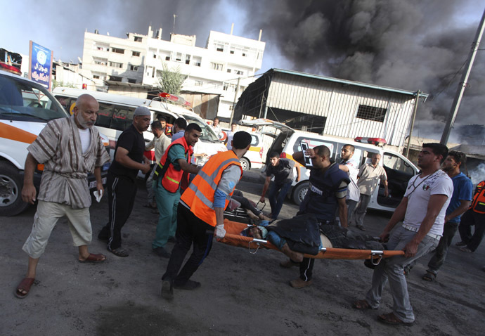 Palestinians carry the body of a local Palestinian journalist, whom medics said was killed by Israeli shelling near a market in Shejaia, as smoke rises in the east of Gaza City July 30, 2014. (Reuters/Ashraf Amrah)